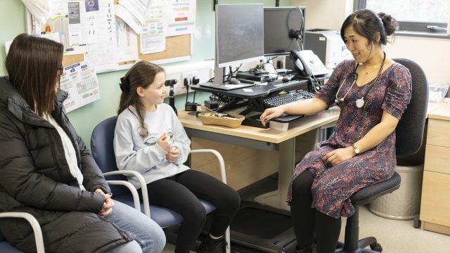 Doctor consulting with patient and mother in office.